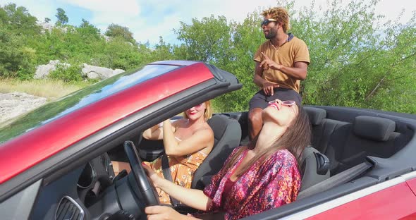 Handsome black man sitting on hood of convertible dancing with friends, graded alt