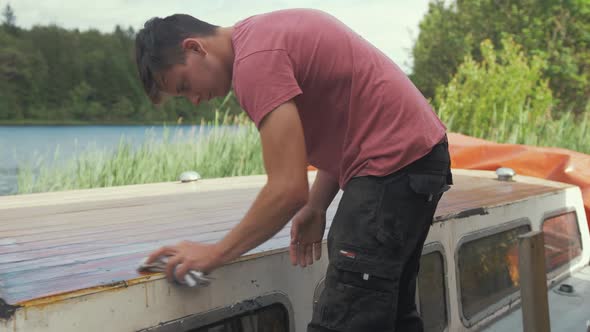 Young man wiping dust off boat roof planking after sanding planking. CLOSE UP. alt