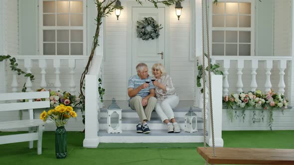 Satisfied Senior Elderly Caucasian Couple Sitting and Drinking Wine in Porch Stairs at Home alt