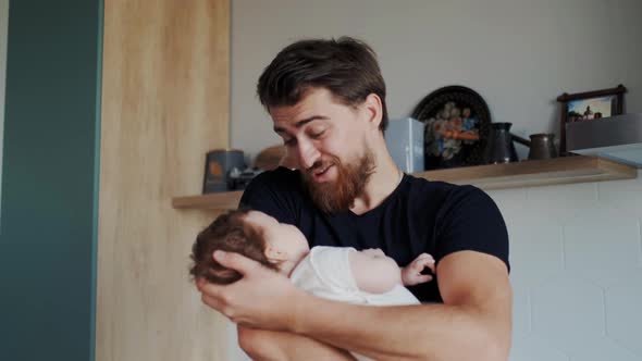 Handsome Bearded Dad Holding a Tiny Infant in His Hands and Showing Affection to Baby alt
