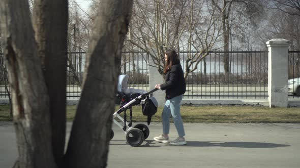 A Young Mother Walks on the Street with a Baby in a Stroller alt