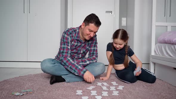 Father and daughter are sitting on the floor in a bright children's room and playing alt