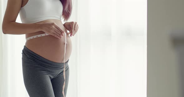 Young Asian Pregnant woman measuring her belly with a tape.