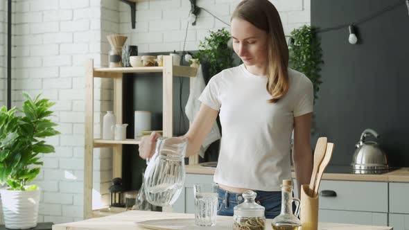 Young Woman Pouring Water From Jug Into Glass in the Kitchen alt