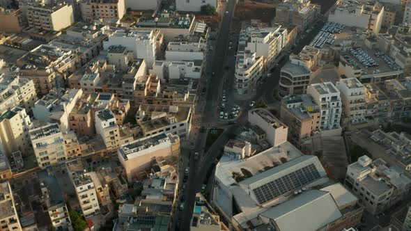 Road Going Through Malta Island City with Beige Brown Buildings in Sunlight, Aerial Drone Crane Up alt