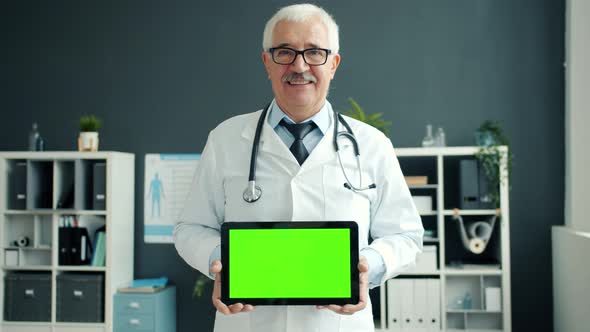 Cheerful Doctor Holding Tablet with Green Chroma Key Screen Smiling in Office in Clinic alt