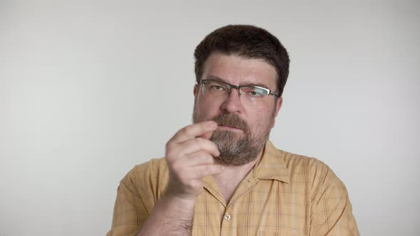 Man with a beard and glasses looks and talks thoughtfully on a gray background. alt