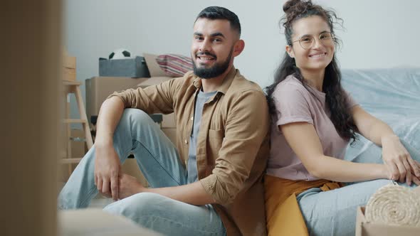 Portrait of Cheerful Mixed Race Couple Smiling Holding Keys Sitting in New House with Boxes Around alt