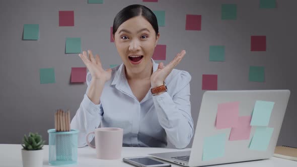 Asian woman happy working at home office looking at camera and smiling surprised.