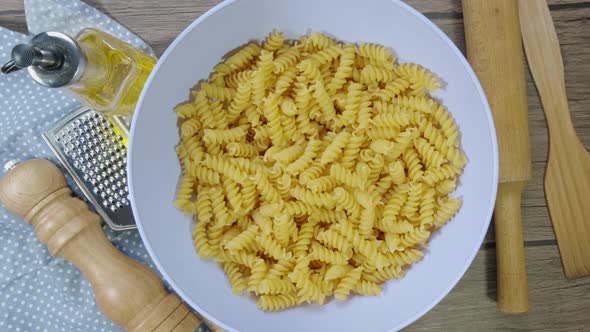 Fusilli Pasta Dry on the Table Slowly Rotates. Blue Plate on Wooden Background. Top View. alt