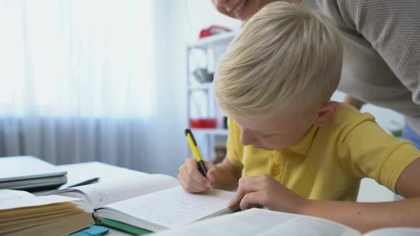 Diligent Male Kid Doing Homework at Desk, Mother Praising Son, Touching Head