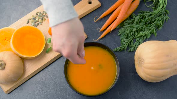 Hand Adding Pumpkin Seeds and Mint Leaf To Soup  alt