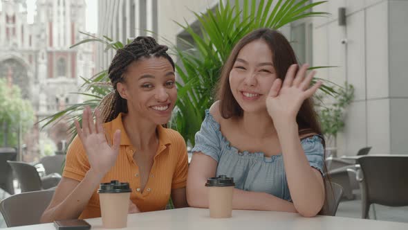 Two Smiling Happy Girlfriends Woman Vlogger Speaking Looking at Camera Sitting in Cafe alt
