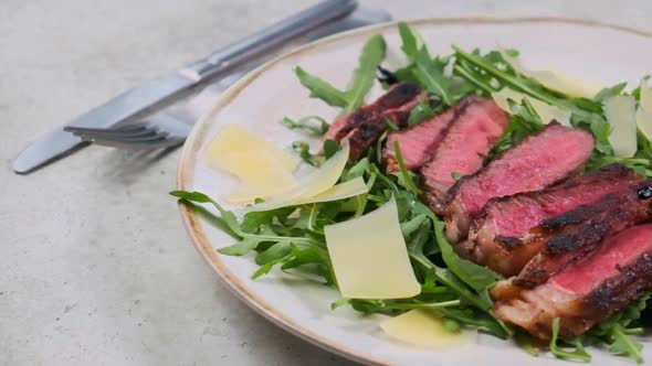 Beef steak tagliata with arugula and parmesan on gray plate, gray background. alt
