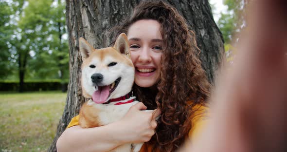 Portrait of Attractive Lady Taking Selfie with Puppy in Park Kissing Hugging Dog alt