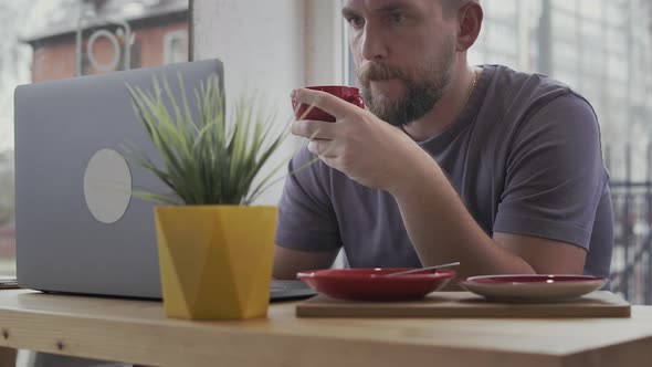 Man Drinking Coffee and Using Laptop