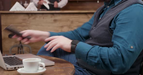 Freelancer in a Pub Finishes a Phone Conversation and Starts Typing on His Laptop alt