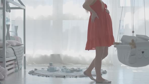 Unrecognizable Pregnant Woman Walking in Future Baby Room Caressing Belly. Young Caucasian Mother alt