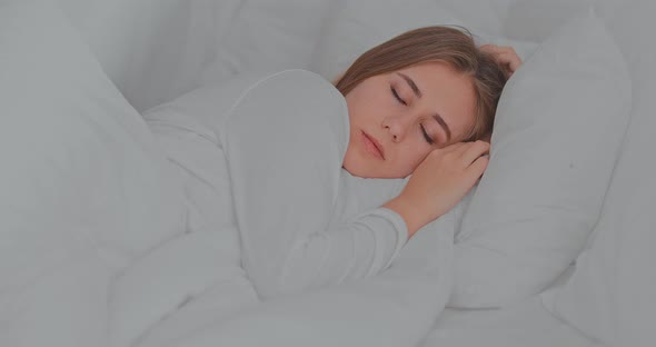 Pretty Girl Sleeps Sweetly in Bed Under a White Blanket on a White Pillow