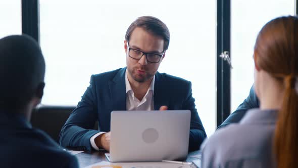 Young people in suits communicating at a business meeting using computer alt