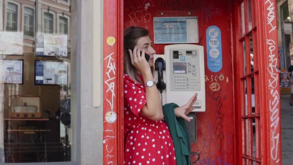 Young Woman Is Standing in Old Red Telephone Box and Talking on Her Gadget alt