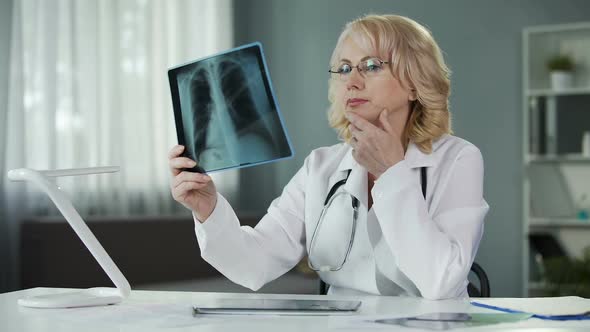 Doctor Examining X-Ray of Patient's Lungs Making Notes in Medical Records alt