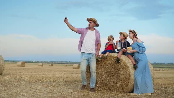 Talking By Phone, Man with His Wife and Male Children Enjoying Picnic in Field with Bales  alt