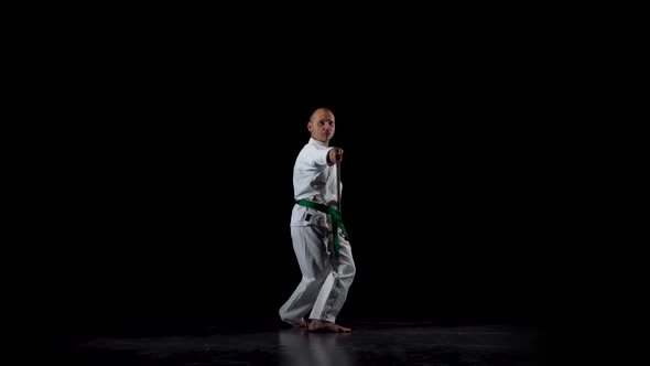 Kendo Fighter on White Kimono Practicing Martial Art with the Bamboo Bokken on Black Background alt
