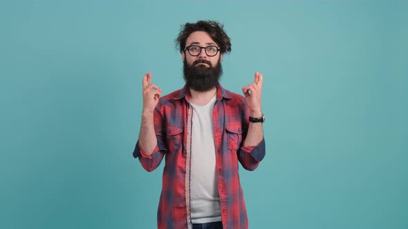 Young Man That Keeps Fingers Crossed Isolated Over Turquoise Background