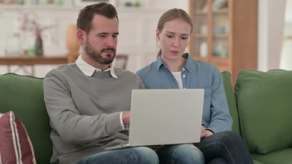 Couple Working on Laptop Together While Sitting on Sofa alt