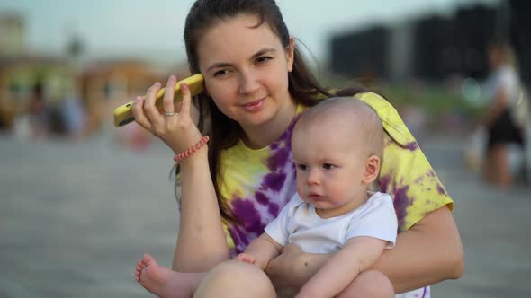 Babysitter with Baby Outdoors Listening to Voice Message From Baby Mom alt