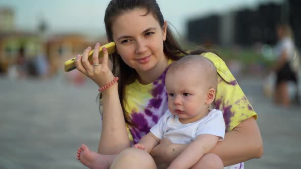 Babysitter with Baby Outdoors Listening to Voice Message From Baby Mom