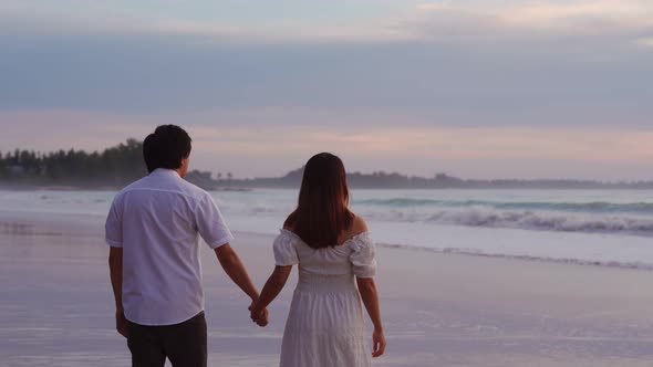 Young Asian couple holding hand together and looking beautiful sunset on the beach