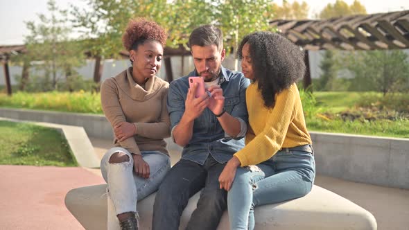 Three friends - a white man and two black women chatting and laughing in park alt