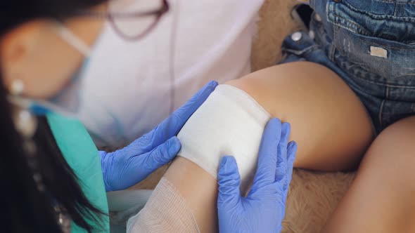 Doctor in Medical Gloves Imposes Sterile Bandage on Injured Knee Wound