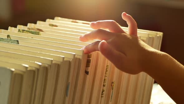 A little cute girl is choosing a book in the bookshelves at home. alt