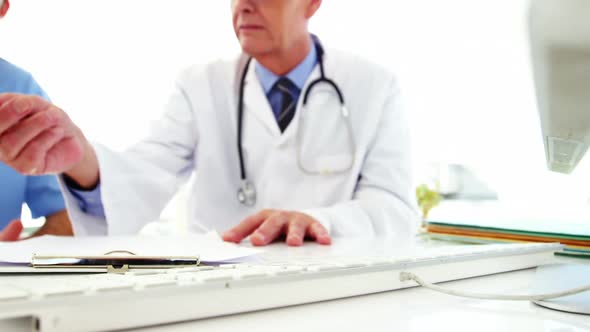 Male doctor and coworker discussing over computer alt