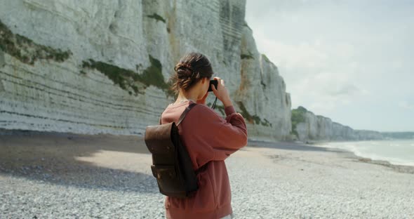 A Young Woman Walks Along a Pebbly Beach Past Sheer Chalk Cliffs alt