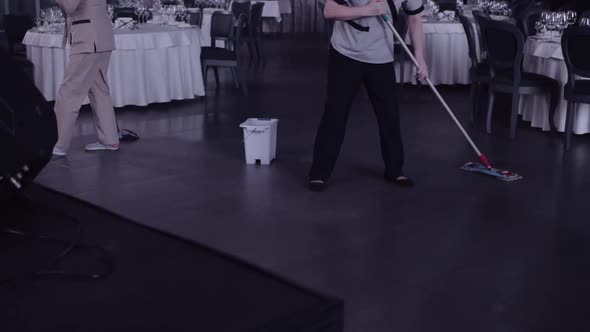 A Woman with a Mop Washes the Floor in the Restaurant