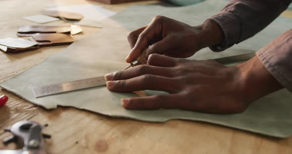 Close up of hands of african american craftsman cutting leather precisely in leather workshop alt
