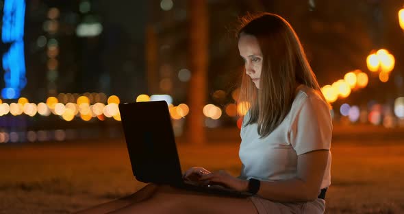 Young Female Student with Laptop at Night in Town Typing Text alt