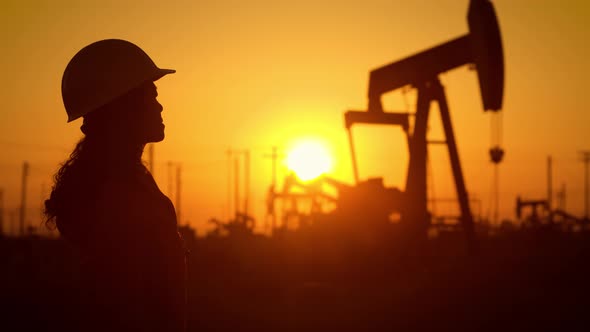 Woman engineer inspects oil pumps at sunrise alt