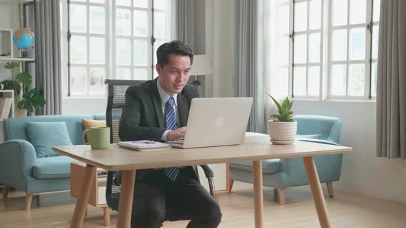 Asian Businessman In Business Suit Typing On Computer While Working At Home alt