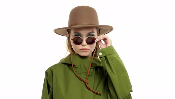 Woman in a Autumn Look in Studio in Green Parka and Hat Turns and Poses To the Camera alt