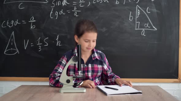 A Little Girl Schoolgirl in a Shirt Stands Against the Background of a Chalk Board alt