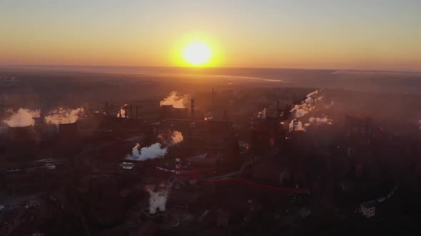 The smoke of a metallurgical plant against the backdrop of the sun at dawn.