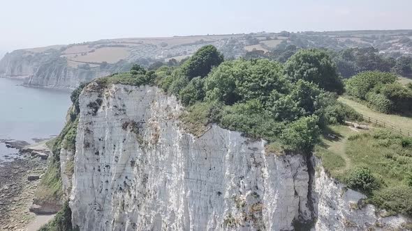 Aerial tilt of a foliage covered cliffside village near the beach on a sunny day. There are several alt