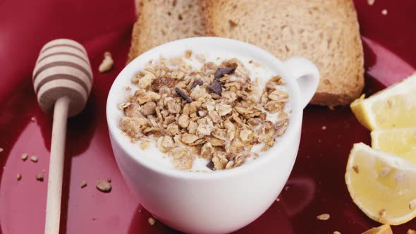 Cup of White Greek Yogurt with Crunchy Granola in a Rotating Red Plate alt