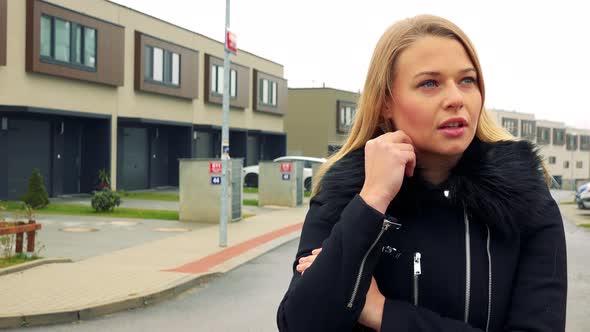 A Young, Beautiful Woman Stands on the Street in a Suburban Area and Broods
