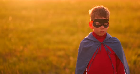 A Child in the Costume of a Superhero in a Red Cloak Runs Across the Green Lawn Against the Backdrop alt